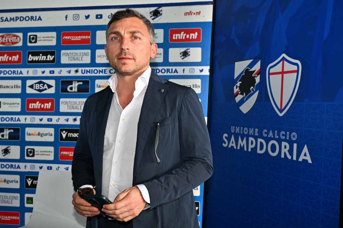 Matteo Manfredi in primo piano e in piedi davanti a un pannello con il logo della Sampdoria