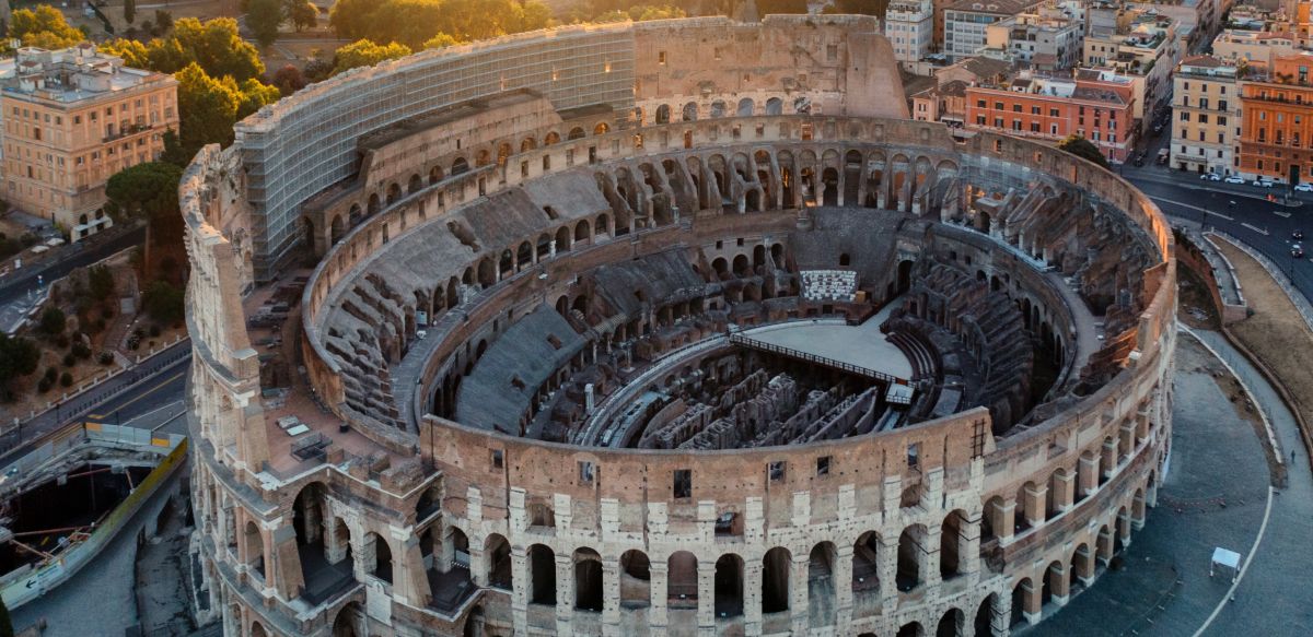 Veduta aerea panoramica del Colosseo a Roma durante il tramonto con i fori imperiali sullo sfondo.